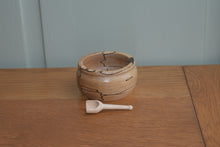 Load image into Gallery viewer, A small handturned wooden bowl with a small handturned wooden scoop lying in front of it on a wooden bench with a pale green background.