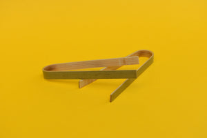 Two pairs of wooden tongs on a yellow background. 