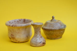 Three individual wooden pieces. A bowl, a vase and a bowl with a lid on a yellow background. 