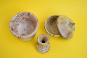 A birds eye view of a wooden bowl, vase and pot with it's lid slightly off on a yellow background. 
