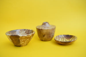 A wooden bowl, a wooden vase and a wooden dish on a yellow background. 