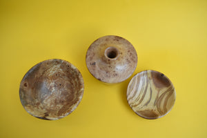 A birds eye view of a wooden bowl, a wooden dish and a wooden vase on a yellow background. 