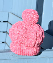 Load image into Gallery viewer, A pink childs hat with a pink pom pom sitting on a light blue bench. 
