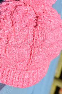A close up of a pink hand knitted childs hat with a cable detail. 