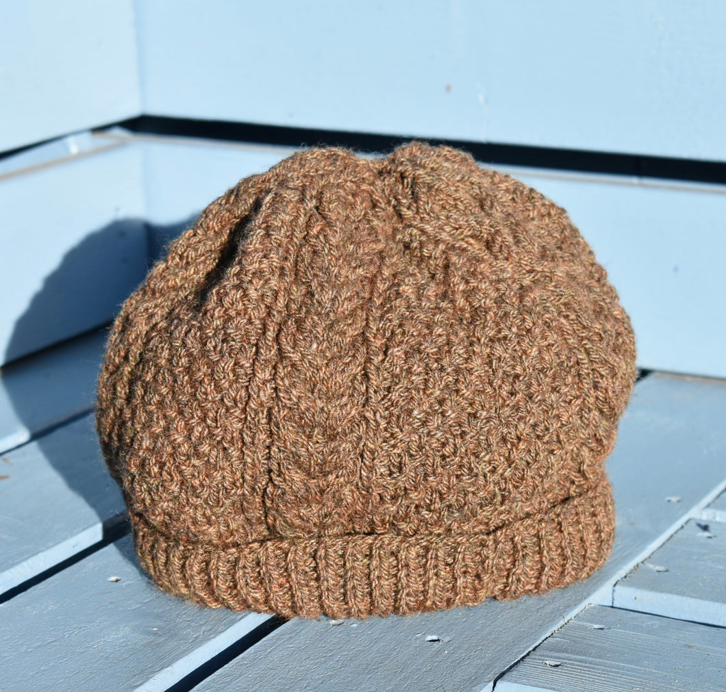 A dark brown hand knitted hat with a cable pattern sitting on a light blue bench. 