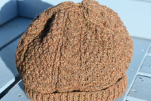 Load image into Gallery viewer, A close up of a dark brown hand knitted hat witha cable patter sitting on a light blue bench. 
