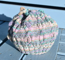 Load image into Gallery viewer, A multi coloured childs knitted hat sitting on a light blue bench. 
