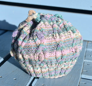 A multi coloured childs knitted hat sitting on a light blue bench. 