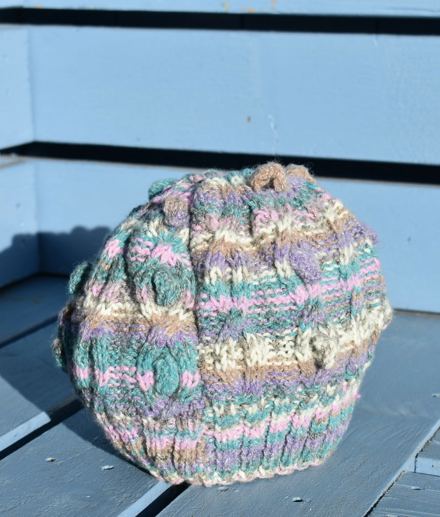 A multi coloured hand knitted hat sits on a light blue bench. 