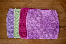 Load image into Gallery viewer, Four brightly coloured square cotton hand knitted cloths lying on a wooden background each slightly overlapping. 
