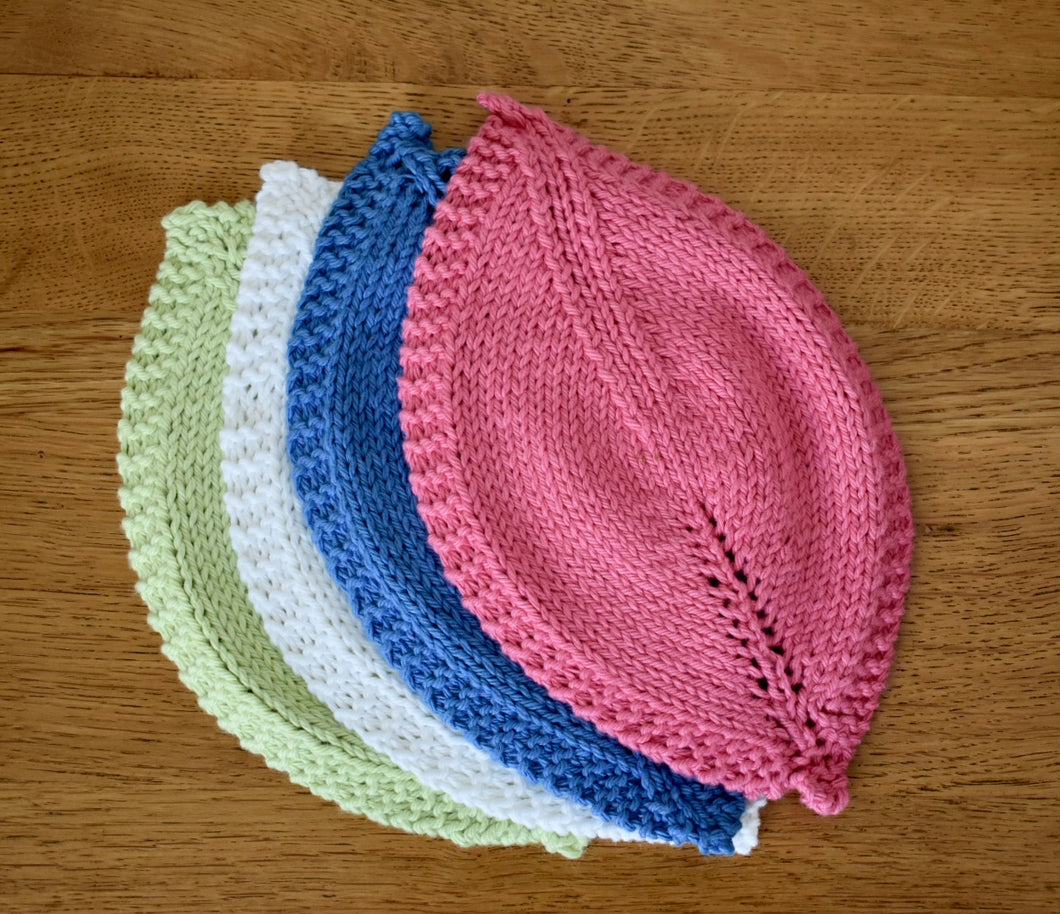 Four coloured hand knitted cotton leaf shaped cloths lying on a wooden background, each slightly overlapping. 