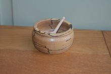 Load image into Gallery viewer, A small handturned wooden bowl with a small wooden scoop in it sitting on a wooden bench with a pale green background.
