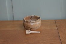 Load image into Gallery viewer, A small handturned wooden bowl with a small handturned wooden scoop lying in front of it on a wooden bench with a pale green background. 
