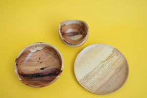 A birds eye view of a wooden set of two bowls and a plate on a yellow background.