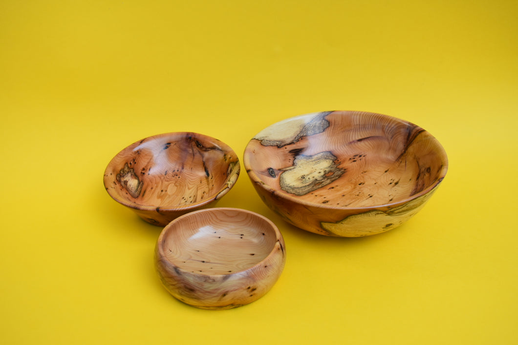 Three wooden bowls of varying sizes on a yellow background.