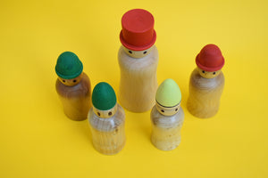 A birds eye view of five wooden peg people wearing hats on a yellow background. 